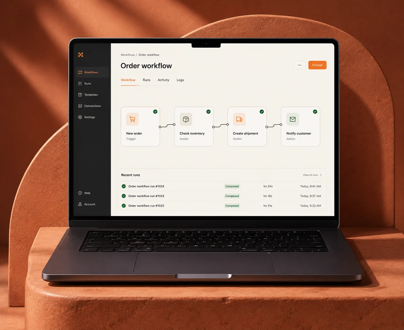 A laptop displaying a connected order workflow and recent automation runs on warm terracotta sculptural blocks.